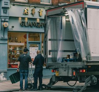 Two men delivering goods to a Chinese store using a truck on a city street.