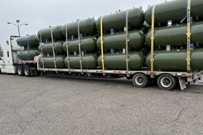 A large stack of wooden planks loaded onto an industrial trailer in an outdoor setting.